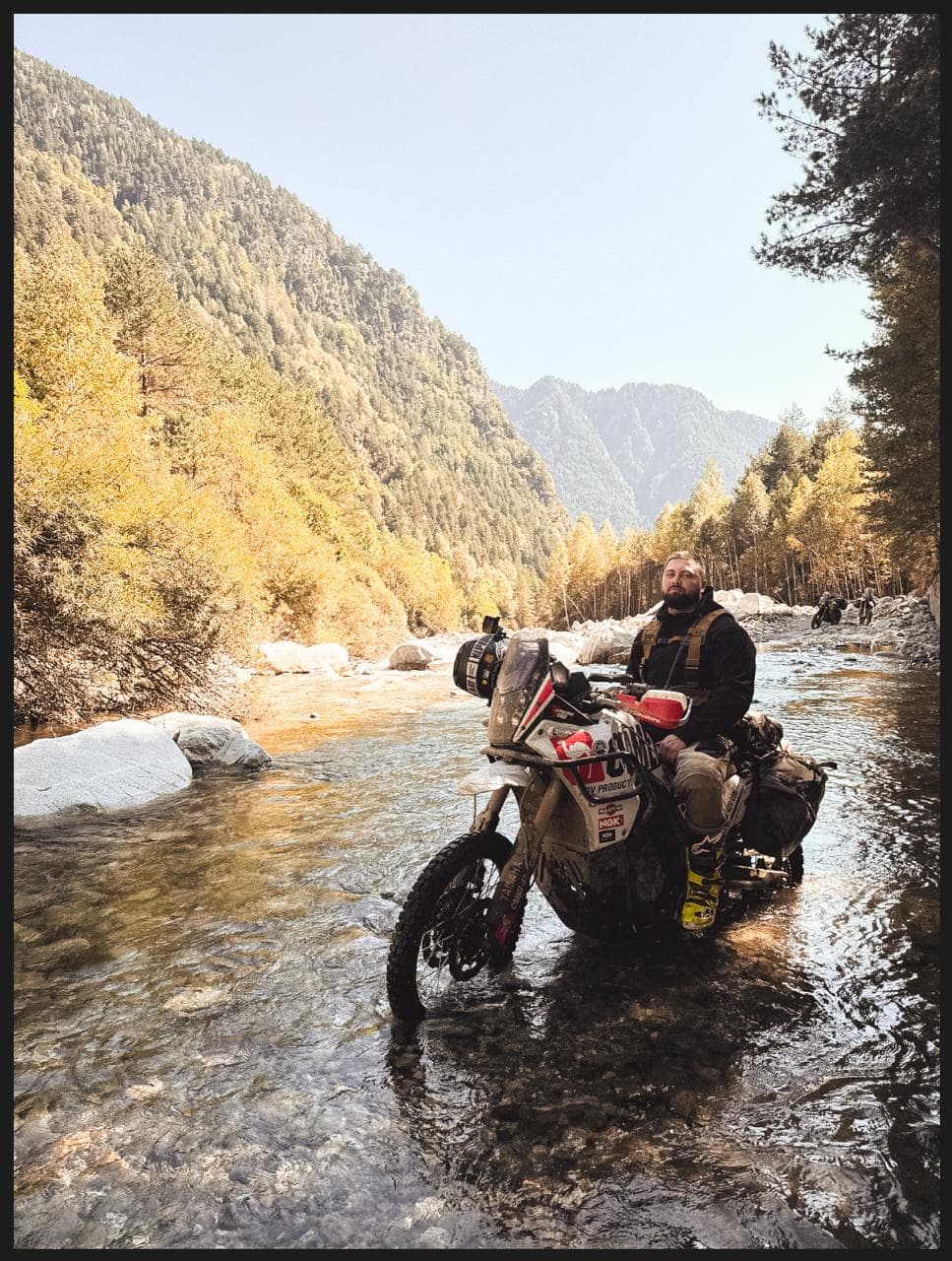 Rider on a loaded adventure bike crossing a river in autumn
